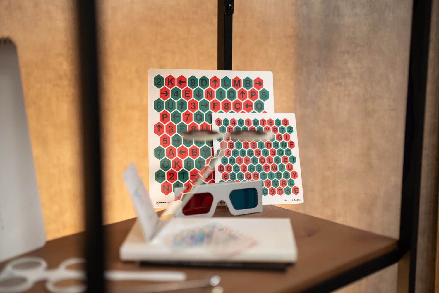 Karten mit Rot-Grün Hexagon-Muster und Zahlen und Buchstaben; davor liegt eine Rot/Blau-Brille